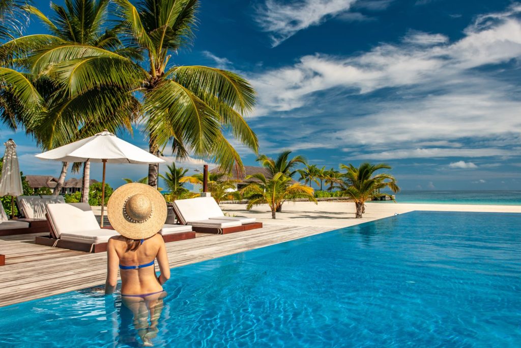 Goedkope last-minute vliegtickets naar een luxe tropisch resort met palmbomen en infinity pool aan het strand.