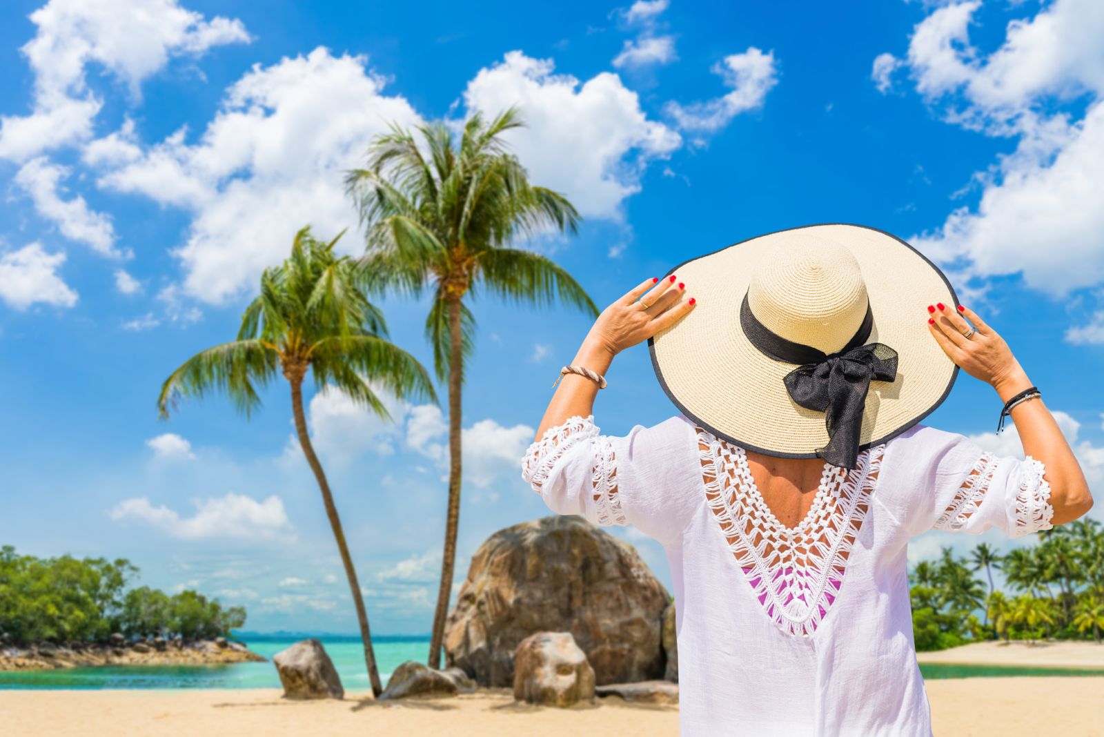 Last minute vakantie naar een tropisch strand met palmbomen, helderblauwe lucht en een vrouw met zonnenhoed.